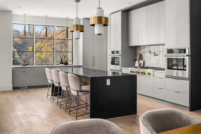 kitchen with a center island, hanging light fixtures, light wood-type flooring, white cabinetry, and stainless steel appliances