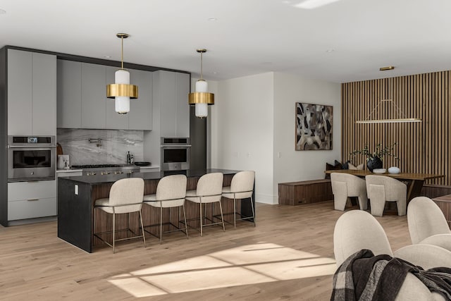 kitchen featuring a breakfast bar, backsplash, gray cabinets, appliances with stainless steel finishes, and light hardwood / wood-style floors