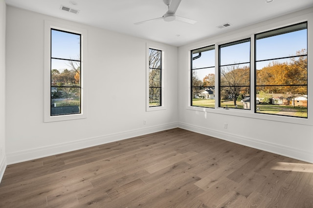 empty room with ceiling fan, a healthy amount of sunlight, and dark wood-type flooring