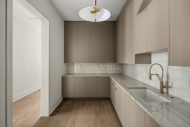 kitchen with light stone countertops, backsplash, sink, pendant lighting, and light hardwood / wood-style flooring