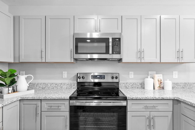 kitchen featuring light stone countertops, appliances with stainless steel finishes, and gray cabinetry