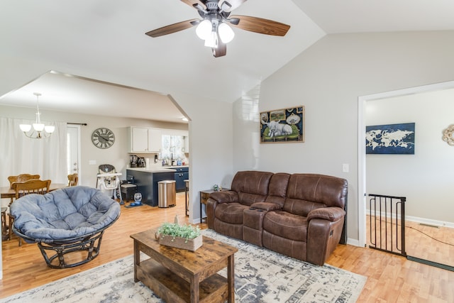 living room featuring ceiling fan with notable chandelier, light wood-type flooring, and lofted ceiling