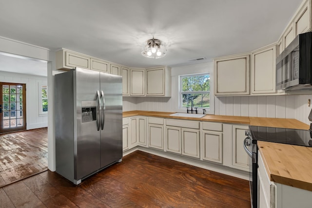 kitchen with butcher block counters, cream cabinetry, appliances with stainless steel finishes, dark hardwood / wood-style floors, and sink