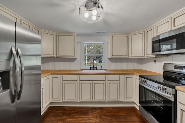 kitchen with butcher block counters, stainless steel appliances, dark wood-type flooring, cream cabinets, and sink