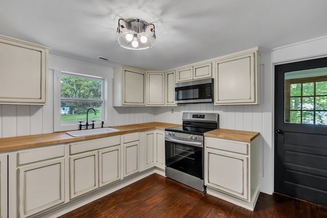 kitchen with appliances with stainless steel finishes, dark wood-type flooring, butcher block counters, sink, and cream cabinetry