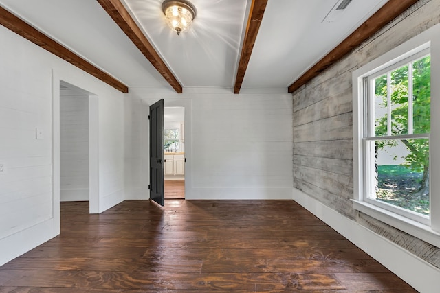 empty room with a wealth of natural light, dark hardwood / wood-style floors, and beamed ceiling