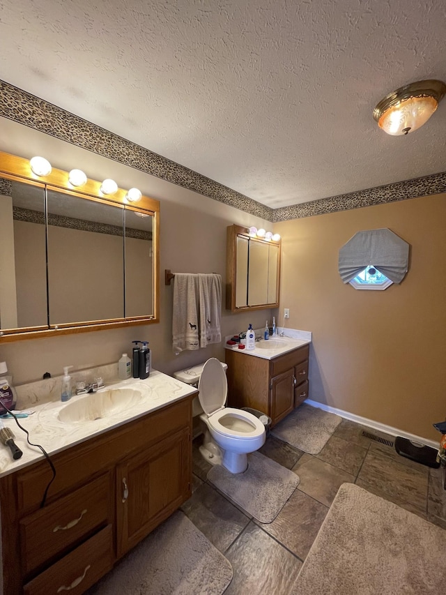 bathroom with two vanities, a sink, a textured ceiling, and baseboards