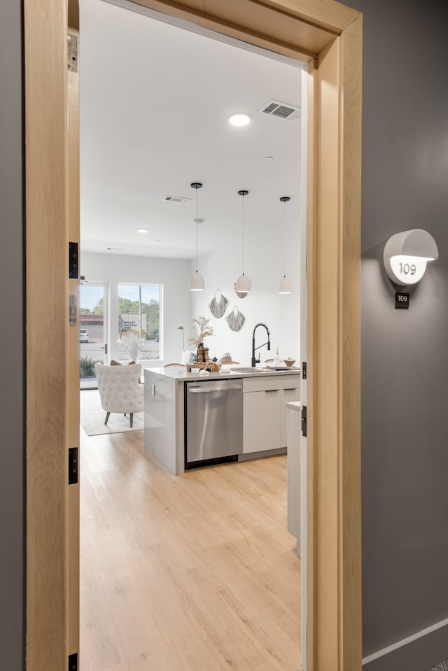 kitchen with stainless steel dishwasher, sink, pendant lighting, light hardwood / wood-style flooring, and white cabinets