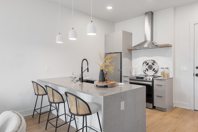 kitchen with hanging light fixtures, sink, wall chimney exhaust hood, light wood-type flooring, and appliances with stainless steel finishes