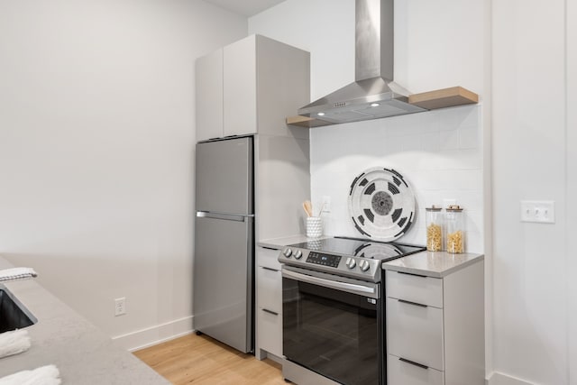 kitchen with wall chimney exhaust hood, appliances with stainless steel finishes, light hardwood / wood-style floors, light stone counters, and white cabinetry