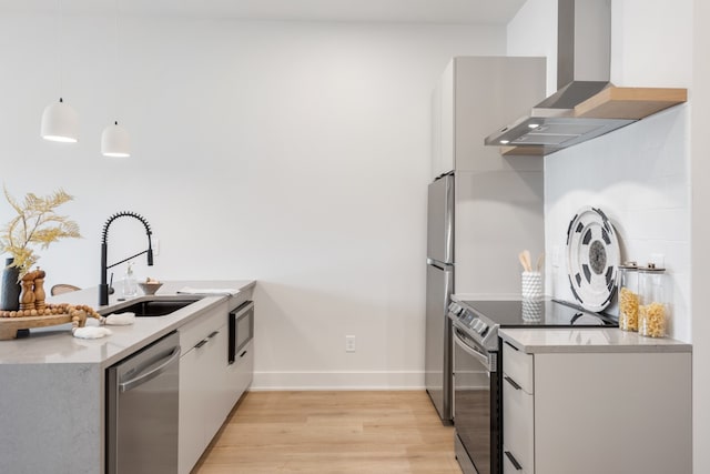 kitchen with wall chimney range hood, hanging light fixtures, light wood-type flooring, white cabinetry, and stainless steel appliances