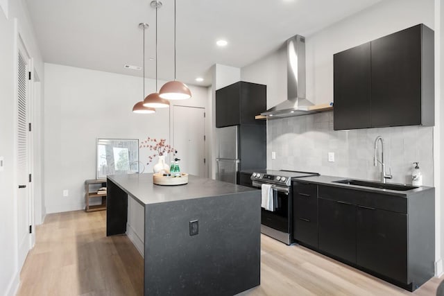 kitchen with light wood-style flooring, dark cabinets, stainless steel appliances, a sink, and wall chimney exhaust hood