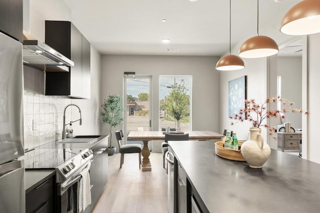 kitchen featuring stainless steel appliances, dark cabinetry, a sink, and backsplash