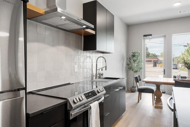 kitchen with stainless steel appliances, visible vents, a sink, dark cabinets, and wall chimney exhaust hood