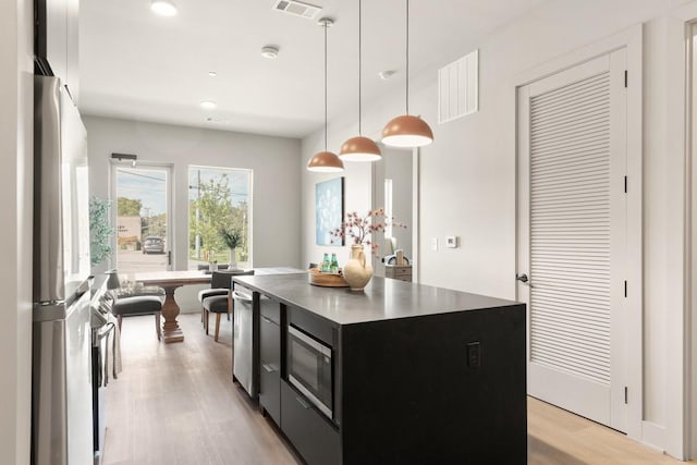 kitchen featuring stainless steel microwave, visible vents, light wood-style floors, freestanding refrigerator, and dark cabinetry