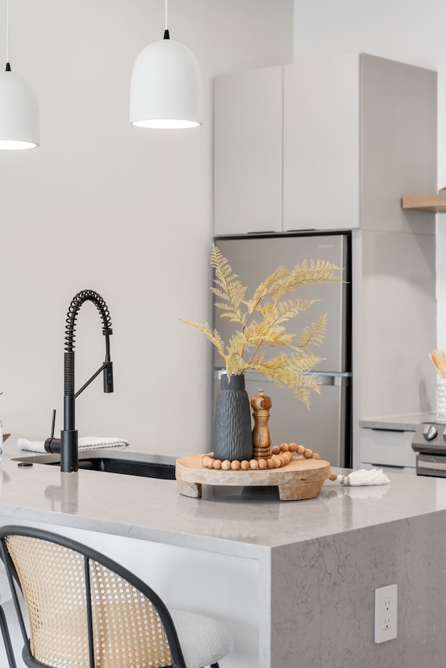 interior details featuring light stone counters, hanging light fixtures, and stainless steel refrigerator