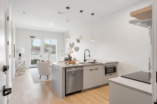 kitchen with appliances with stainless steel finishes, sink, decorative light fixtures, light hardwood / wood-style floors, and white cabinetry