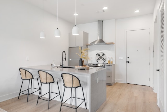 kitchen featuring light wood-type flooring, wall chimney range hood, white refrigerator, white cabinets, and hanging light fixtures