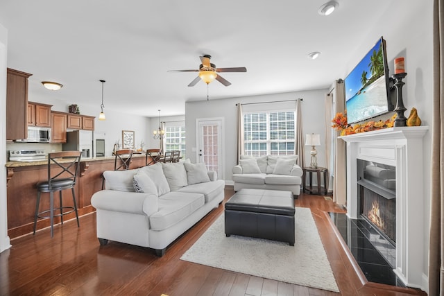 living room with ceiling fan with notable chandelier, dark hardwood / wood-style flooring, and a tiled fireplace