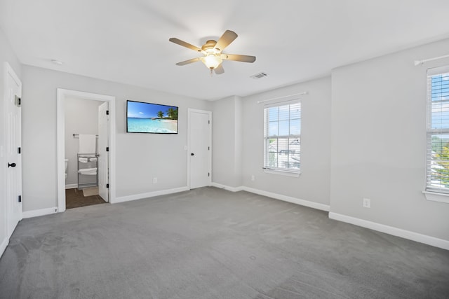 unfurnished bedroom featuring multiple windows, ceiling fan, carpet floors, and connected bathroom