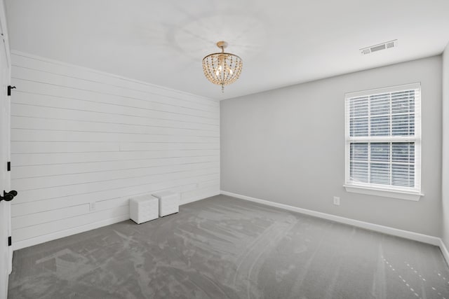 carpeted spare room featuring an inviting chandelier