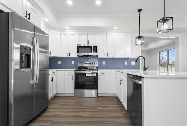 kitchen featuring a peninsula, dark wood-type flooring, white cabinets, appliances with stainless steel finishes, and crown molding