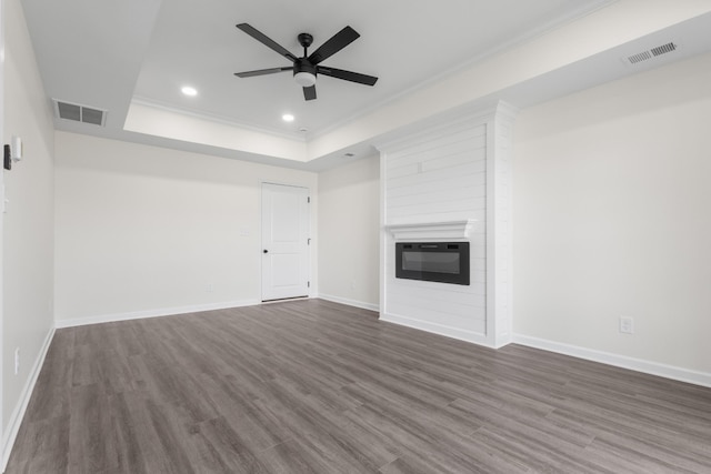 unfurnished living room with dark wood finished floors, visible vents, a large fireplace, and a tray ceiling