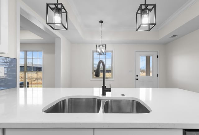 kitchen with a wealth of natural light, ornamental molding, a sink, white cabinets, and a raised ceiling