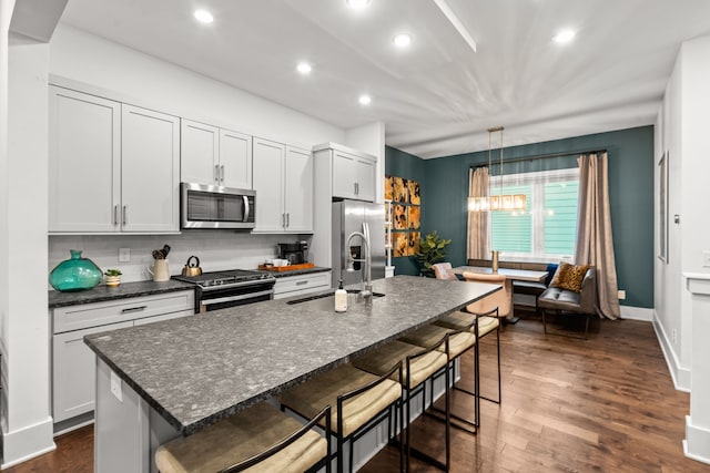 kitchen with white cabinets, a center island with sink, a kitchen bar, dark wood-type flooring, and stainless steel appliances