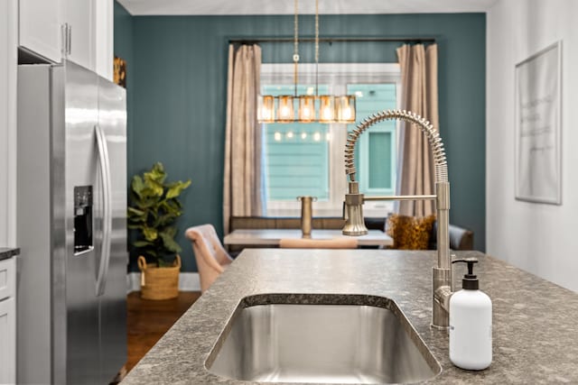 kitchen with sink, dark hardwood / wood-style flooring, hanging light fixtures, stainless steel fridge, and white cabinets