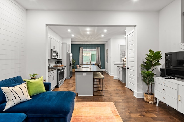 kitchen featuring a kitchen island with sink, dark hardwood / wood-style floors, a kitchen breakfast bar, white cabinets, and appliances with stainless steel finishes