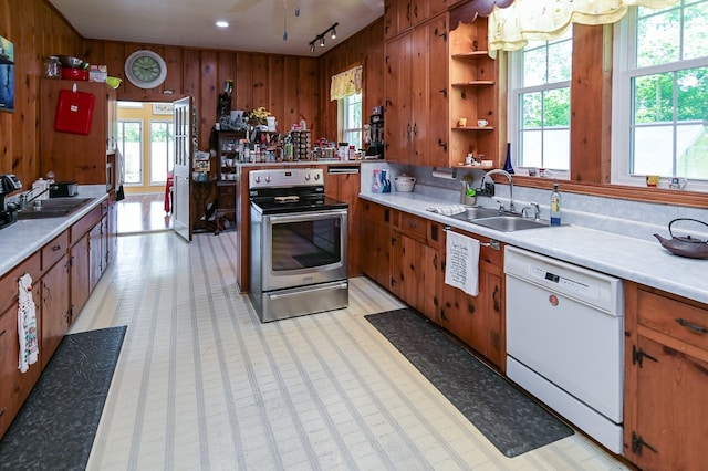 kitchen with dishwasher, stainless steel electric range oven, sink, and wooden walls