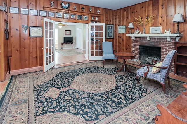 living room with french doors, a brick fireplace, ceiling fan, and wood walls