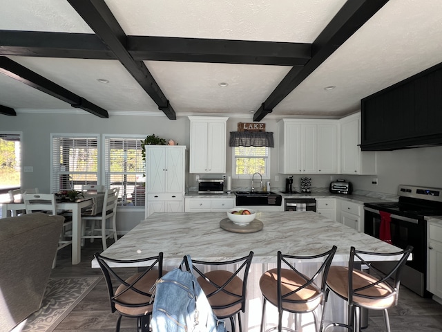 kitchen with stainless steel electric range, beamed ceiling, a healthy amount of sunlight, and a center island