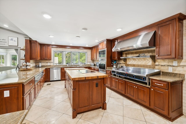 kitchen with light tile patterned flooring, backsplash, wall chimney range hood, appliances with stainless steel finishes, and a center island