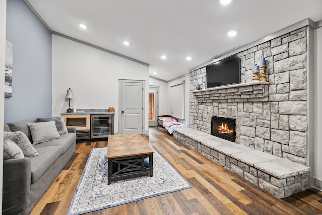 living room featuring a fireplace, wood-type flooring, ornamental molding, and vaulted ceiling