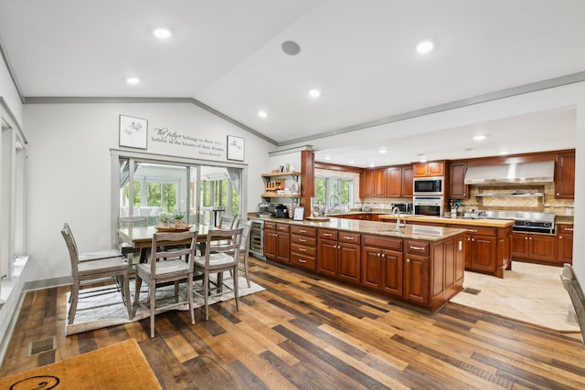 kitchen with a center island with sink, wall chimney exhaust hood, stainless steel appliances, vaulted ceiling, and a healthy amount of sunlight