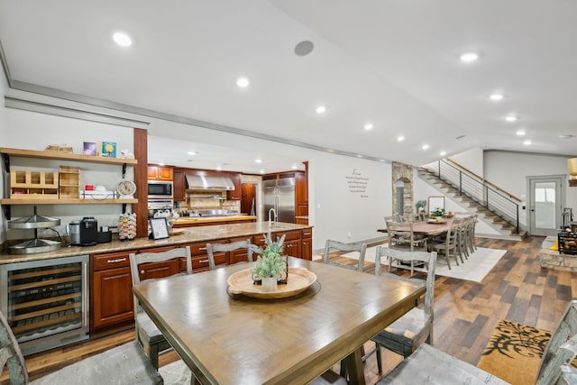 dining space with wine cooler, vaulted ceiling, bar area, and light hardwood / wood-style flooring