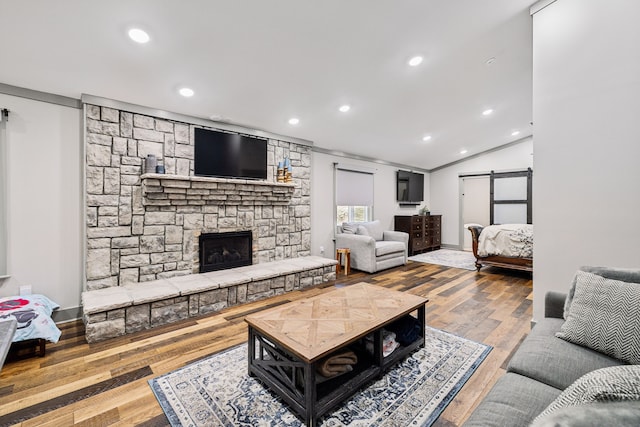 living room featuring wood-type flooring, a stone fireplace, ornamental molding, and a barn door