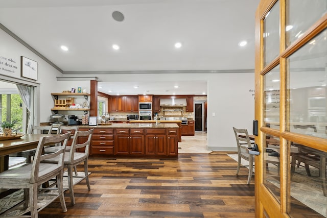 kitchen with wall chimney exhaust hood, dark wood-type flooring, stainless steel appliances, crown molding, and decorative backsplash