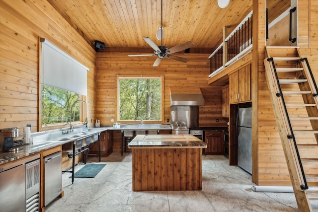 kitchen with extractor fan, wooden walls, a center island, and stainless steel appliances