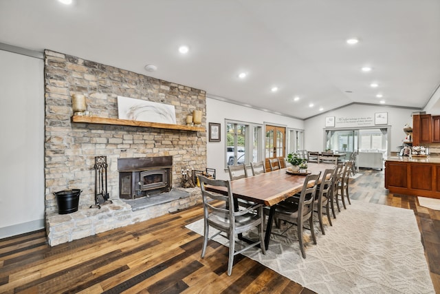 dining area featuring wood-type flooring, crown molding, vaulted ceiling, and a wood stove