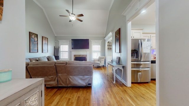 living room featuring light wood-type flooring, ceiling fan, a tile fireplace, vaulted ceiling, and ornamental molding