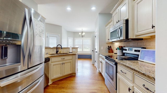 kitchen with light wood-type flooring, stainless steel appliances, sink, pendant lighting, and an inviting chandelier