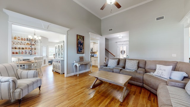 living room featuring ceiling fan with notable chandelier, light wood-type flooring, crown molding, and a towering ceiling