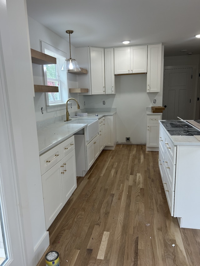 kitchen with hanging light fixtures, white cabinetry, sink, and wood-type flooring