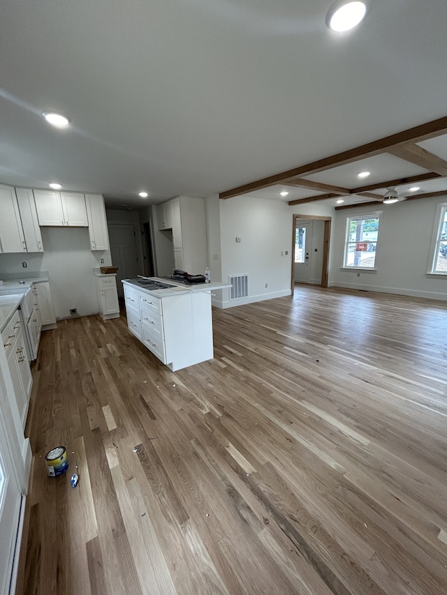 kitchen with white cabinets, a center island, light wood-type flooring, and beamed ceiling