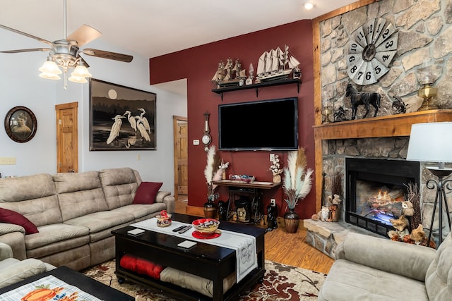 living room featuring ceiling fan, hardwood / wood-style flooring, and a stone fireplace