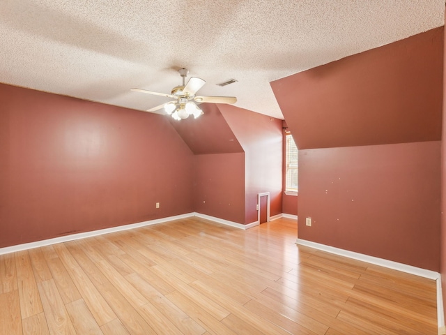 additional living space with lofted ceiling, a textured ceiling, light hardwood / wood-style floors, and ceiling fan