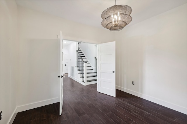 spare room with dark wood-type flooring and a chandelier